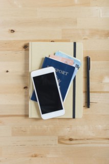 Diary, passport with paper currency, smart phone and pen on wooden table