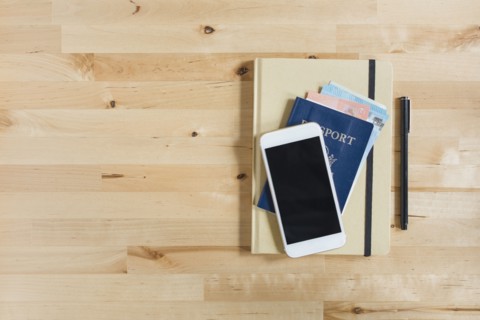 Diary, passport with paper currency, smart phone and pen on wooden table