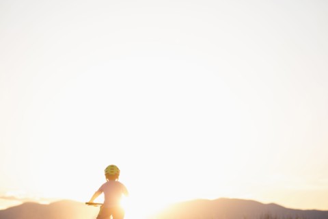 Rear view of boy (8-9) cycling at sunset
