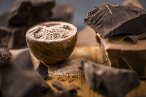Ground chocolate in wooden bowl next to chunk of chocolate