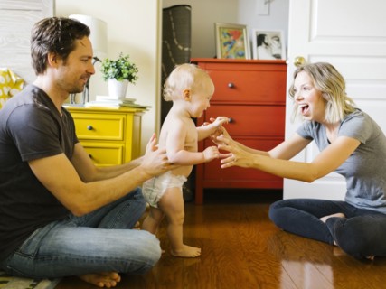 Baby boy (12-17 months) taking first steps with parents at home