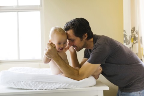 Father playing with baby boy (12-17 months) on changing mat