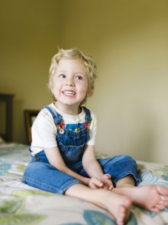 Smiling boy (4-5) sitting on bed and looking away
