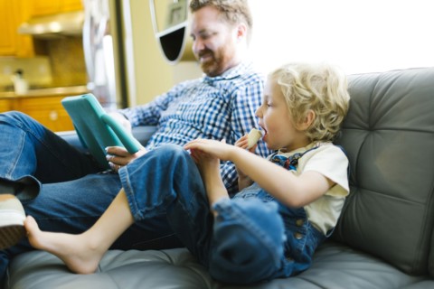 Boy (4-5) and man using digital tablet on sofa in living room