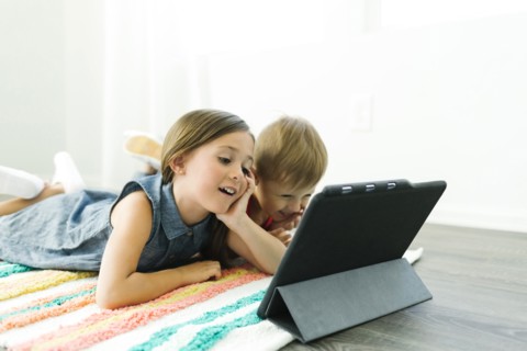 Siblings (2-3, 6-7) lying down on carpet and watching digital tablet