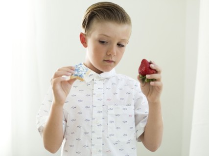 Boys (6-7) holding strawberry and cookie in hands