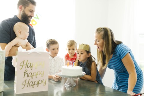 Parents with children (6-11 months, 2-3, 6-7) looking at daughter (6-7) blowing birthday candles