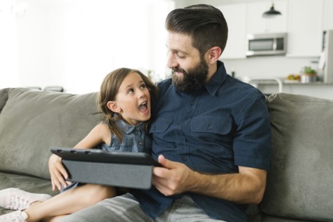 Father with daughter (6-7) using digital tablet in living room
