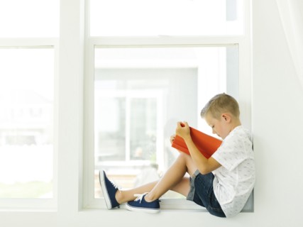 Boy (6-7) reading book by window