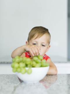 Boy (2-3) picking up grape from bowl