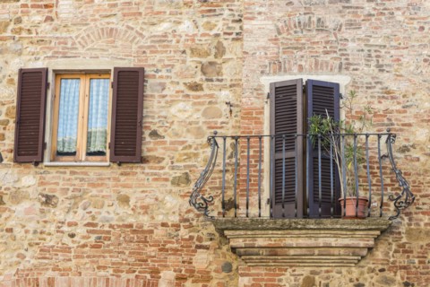 Italy, Tuscany, Montepulciano, Stony and brick facade of house with carved metal balcony and latticed sun blinds