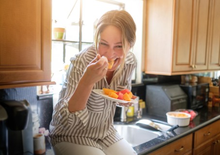 Woman in kitchen eating fruit salad