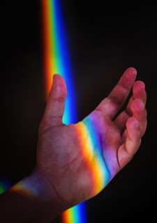 Man's hand with rainbow light against black
