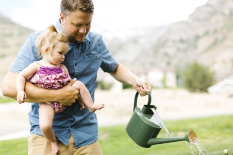 Father with baby girl (12-17 months) watering plants in backyard