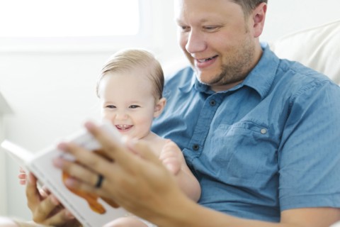 Father with baby girl (12-17 months) sitting in living room and reading book