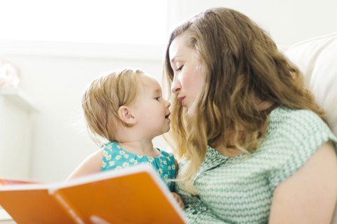 Mother with baby girl (12-17 months) sitting in living room and reading book
