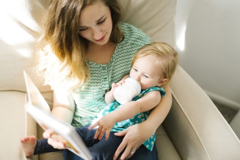 Mother with baby girl (12-17 months) sitting in living room and reading book