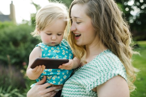 Mother carrying daughter (12-17 months), daughter playing on smartphone