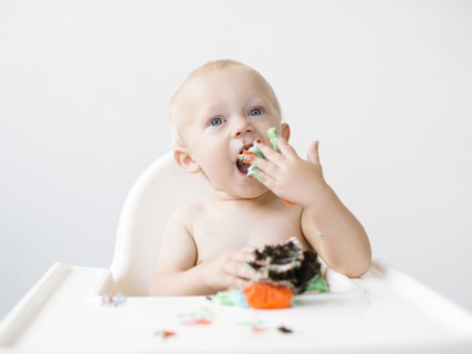 Baby boy (12-17 months) sitting in high chair and eating cupcake