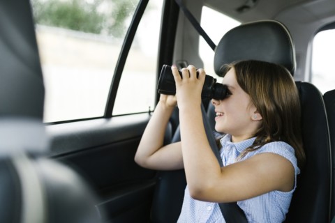 Girl ( 8-9) sitting in car and looking through binoculars
