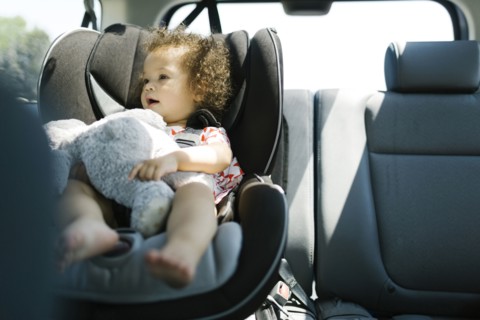 Girl (12-17) sitting on car seat and holding plush toy