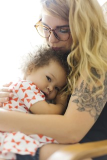 Mother sitting on chair and embracing daughter (12-17 months)