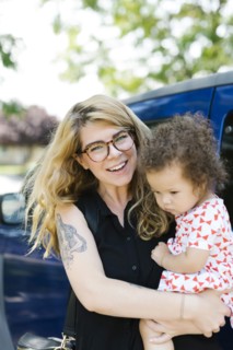 Mother carrying daughter (12-17 months) in front of car