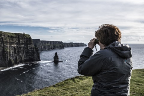 Ireland, Clare County, Woman looking through binoculars on Cliffs of Moher