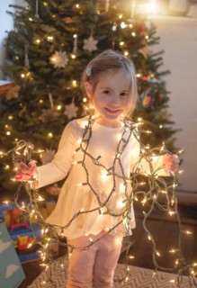 Little girl (4-5) wrapped with christmas lights in living room