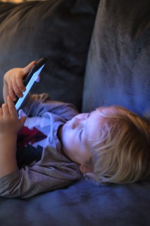 Little boy (2-3) lying down and playing game on smart phone