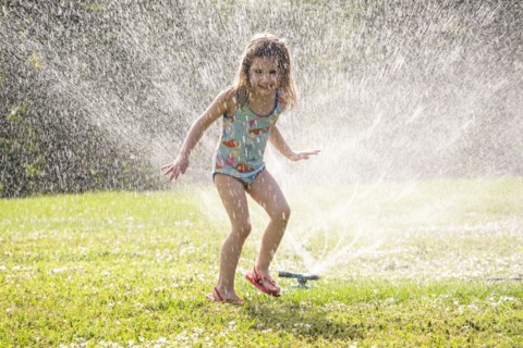 Girl (4-5) splashing in sprinkler water on lawn