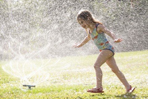 Girl (4-5) splashing in sprinkler water on lawn