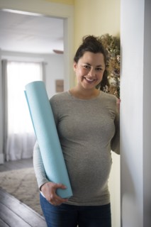 Pregnant woman standing in doorway and holding exercising mat