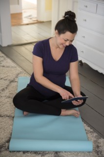Pregnant woman sitting on yoga mat and using tablet pc