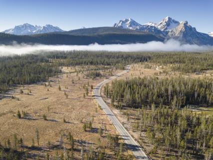 USA, Idaho, Sawtooth Range, Road in forest with snowcapped mountains in background