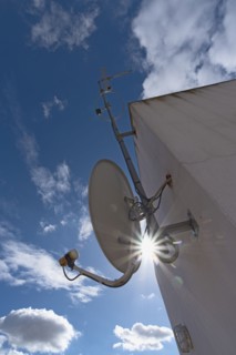 Sun shining through space between satellite dish and facade