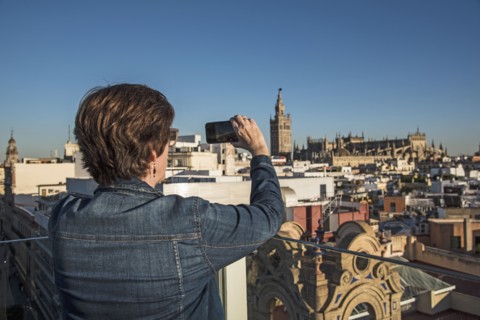 Spain, Andalusia, Seville, Plaza Nueva, Woman taking photo of cityscape and la Giralda with smartphone