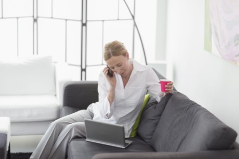 Woman talking on phone and using laptop in living room