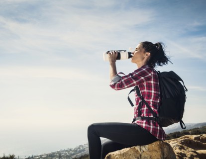 Woman on hike drinking water while sitting on rock