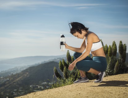 Woman in sportswear crouching with water bottle