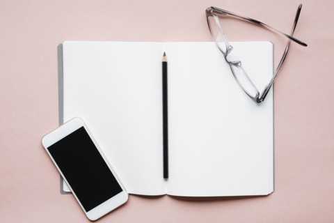 Smart phone, pencil and glasses on open notebook