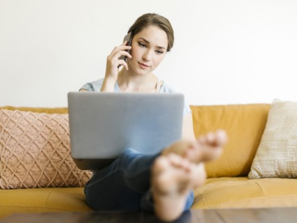 Woman using laptop and smart phone on sofa