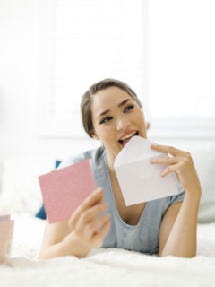 Woman licking envelope on bed