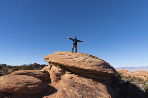 Man with arms outstretched on rock in Arches National Park, Utah, USA
