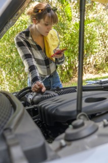 Woman reading on smart phone while repairing car