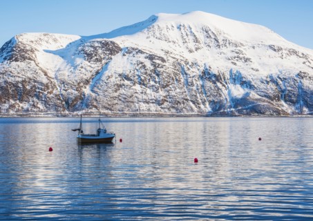 Fishing boat by snow covered mountain in Tromso, Norway