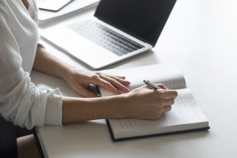 Hand of young businesswoman writing notes at desk