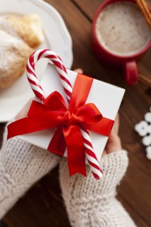 Hands of woman holding Christmas present with candy cane