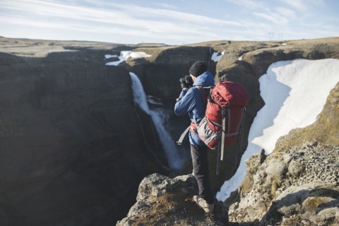 Hiker with backpack on cliff by Haifoss waterfall in Iceland