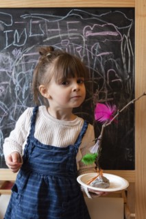 Girl holding stick and feather craft by blackboard
